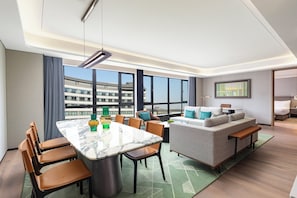 Une chambre d’hôtel moderne dotée d’un coin repas, d’un canapé et d’une grande fenêtre donnant sur la ville.
