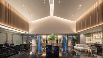 A modern lobby with a reception desk, seating area, and a central plant.