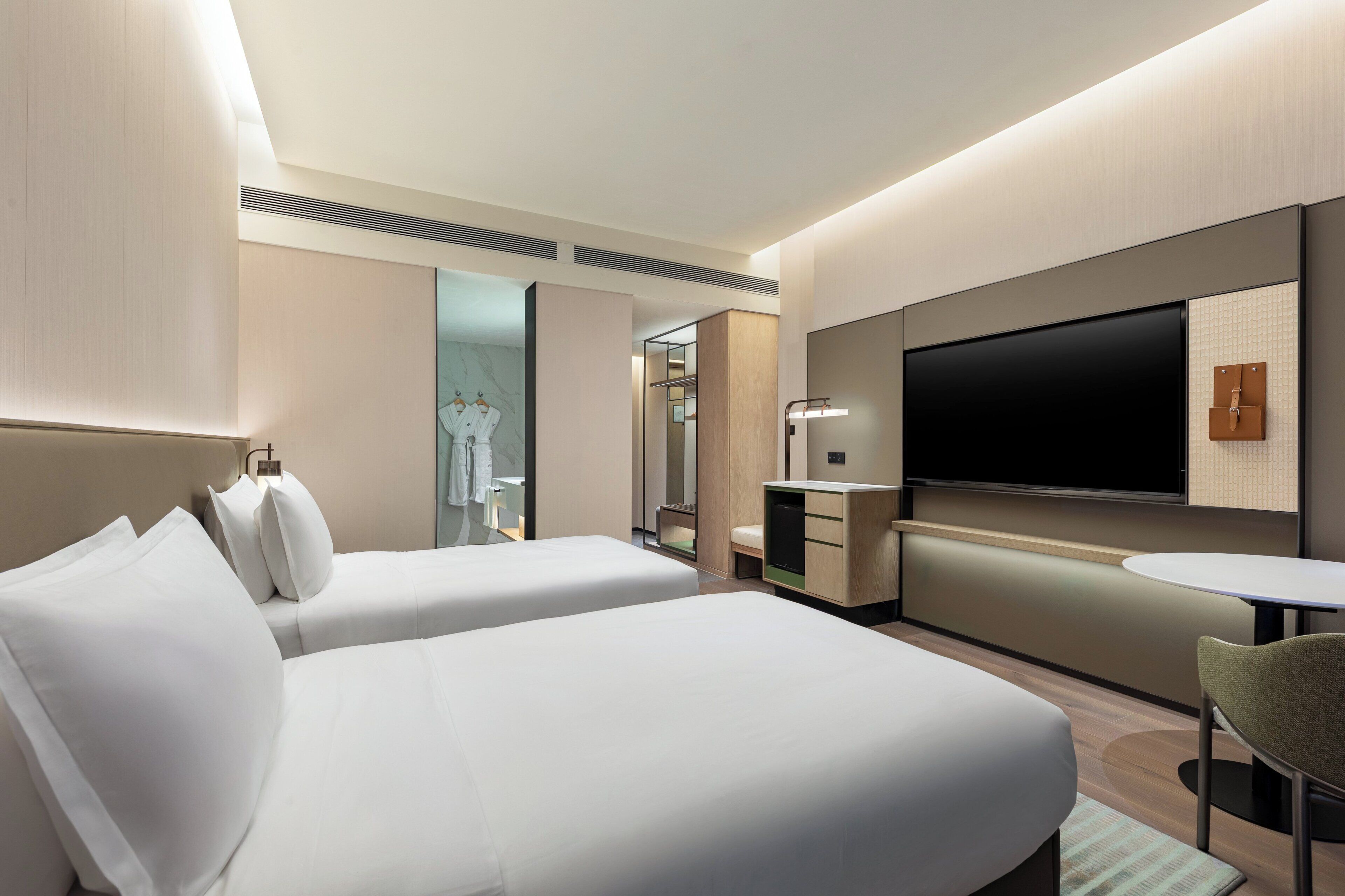 A modern hotel room with two beds, a TV, a small table, and a chair.