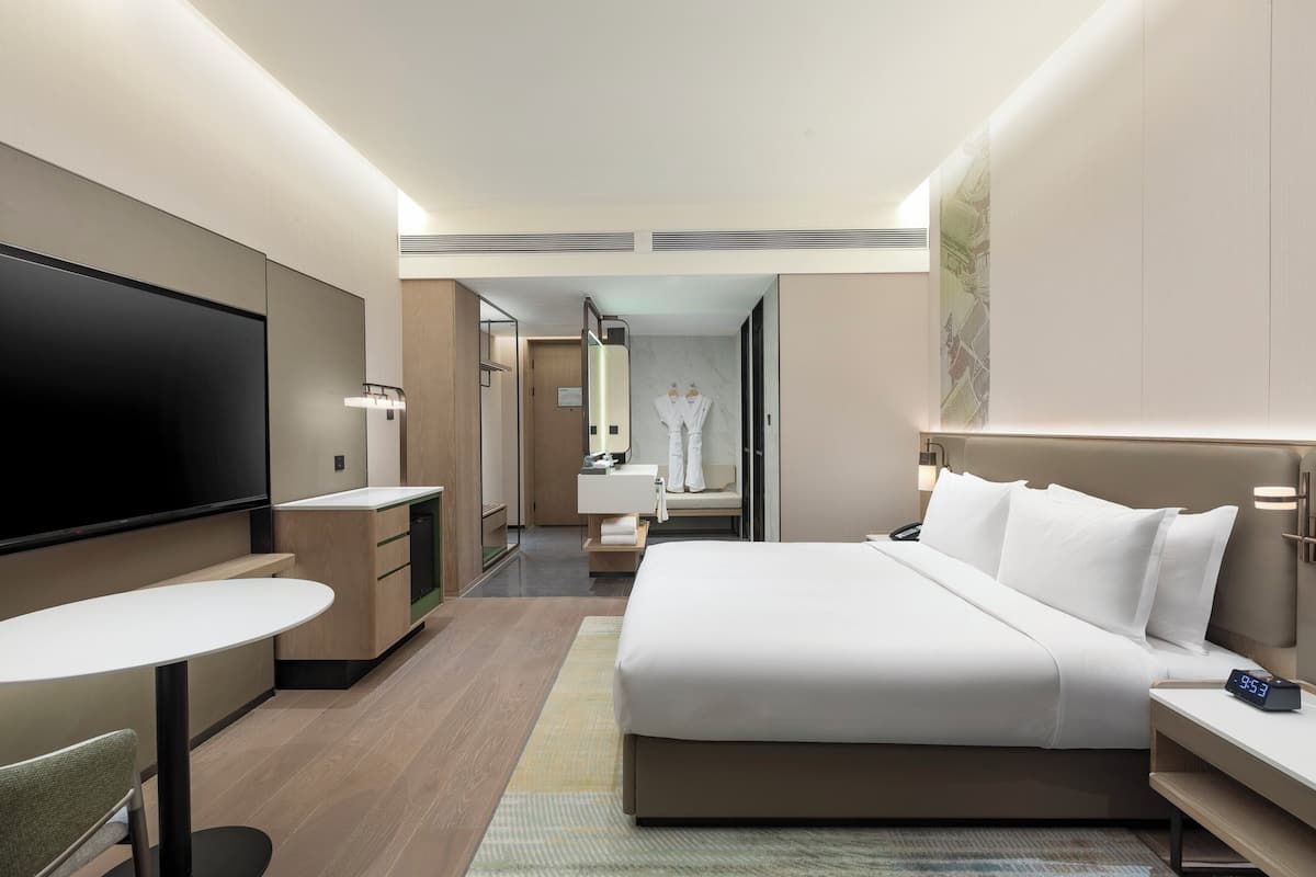 A modern hotel room with a large bed, a flat-screen TV, a desk, and a seating area.