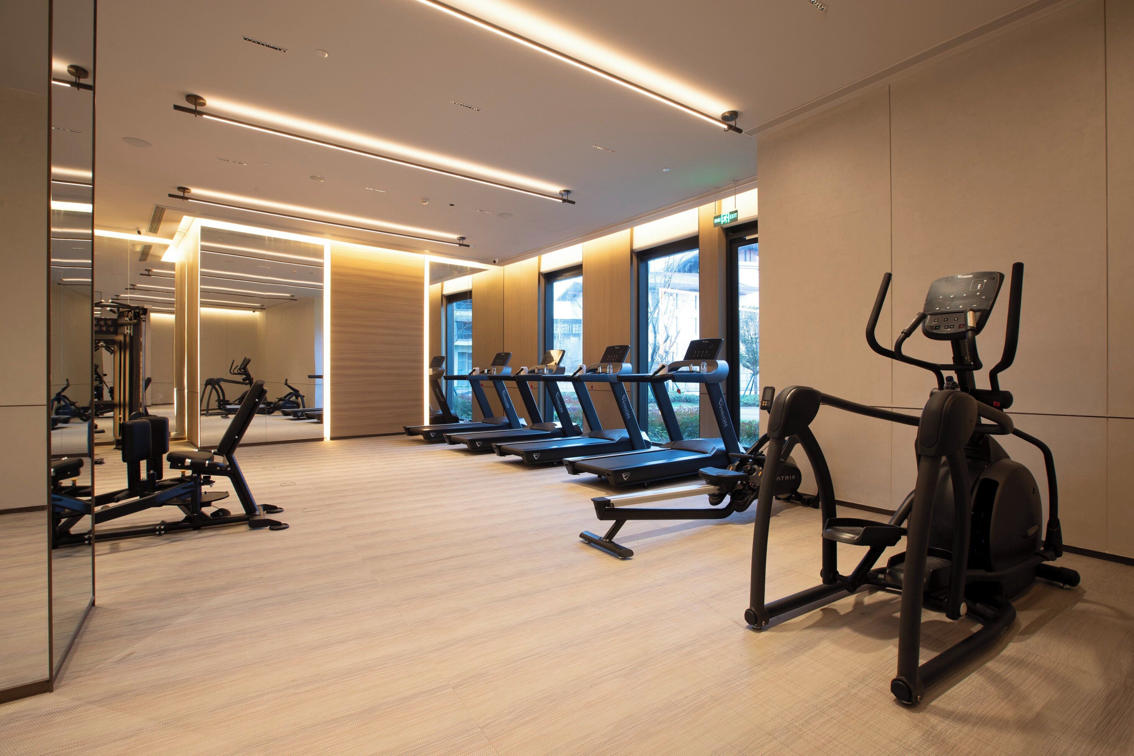 Een sportschool met loopbanden, trainingsfietsen en een spiegelwand.