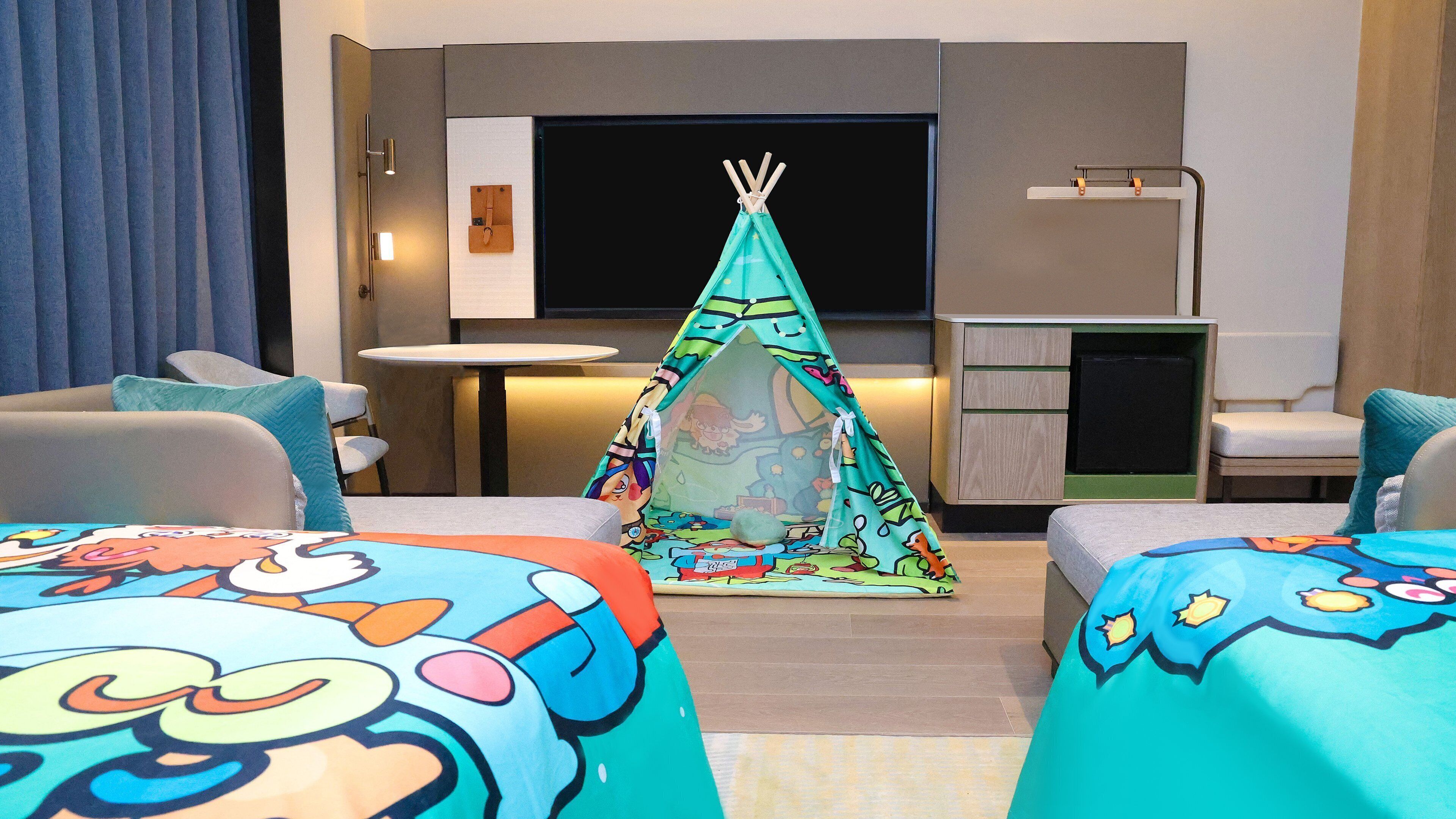 A hotel room with two beds, a small kitchenette, a TV, and a tent-like play area.