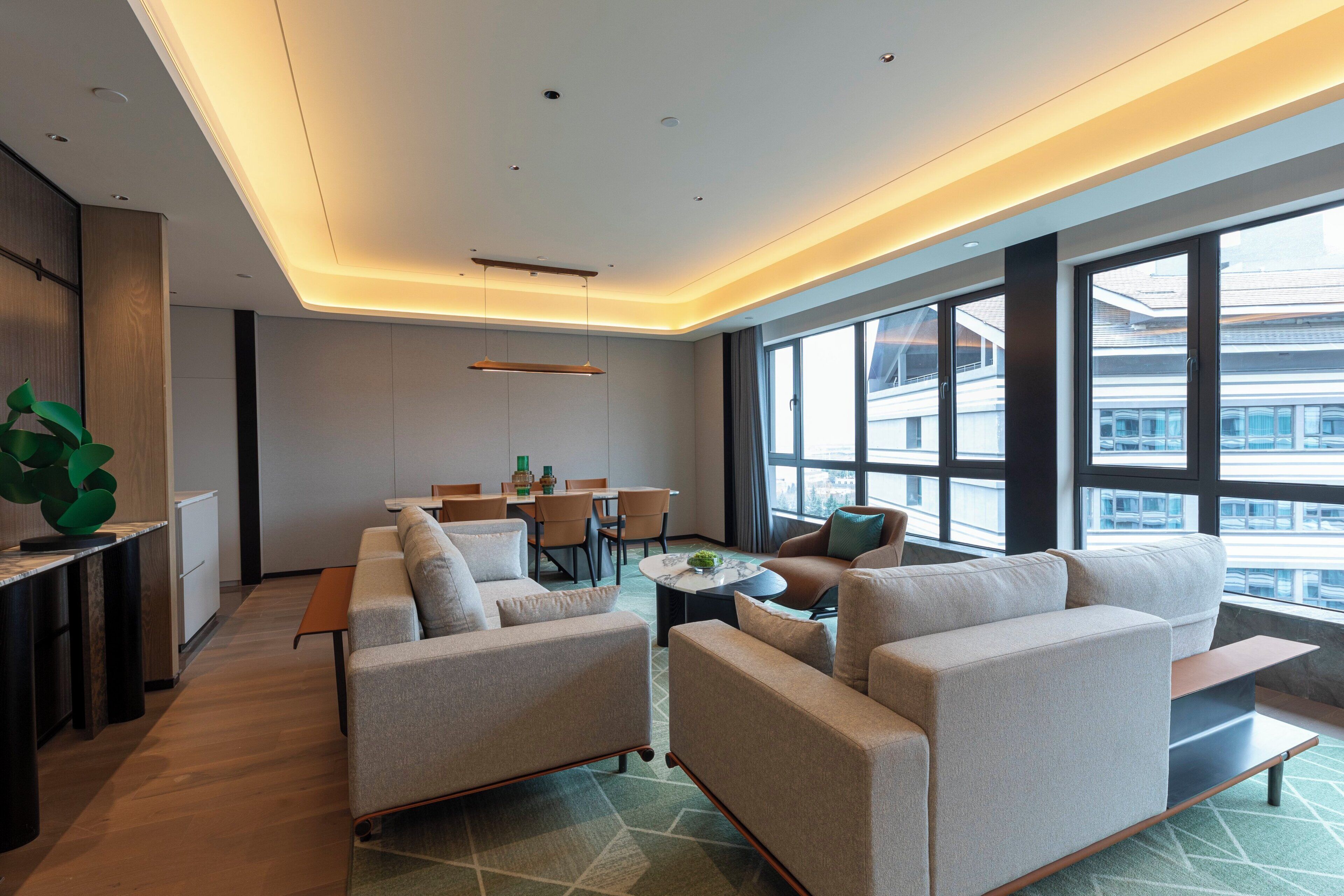 A modern hotel lobby with a sofa set, a dining area, and large windows offering a city view.