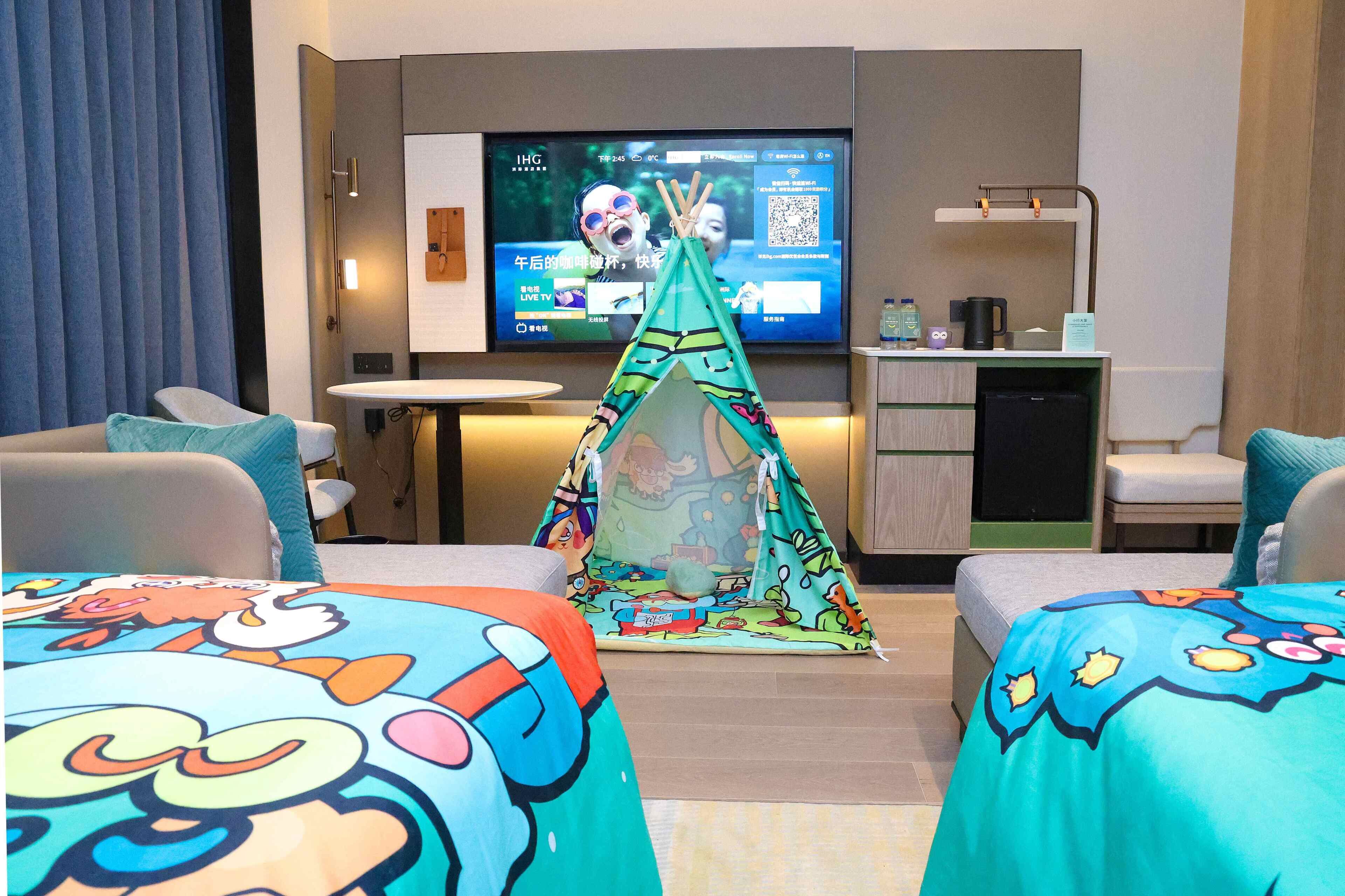 A hotel room with two beds, a TV, a small kitchenette, and a tent-like structure in the center.