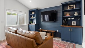 Een woonkamer met een bruine leren bank, een flatscreen televisie aan de muur en een blauwe inbouwkast met diverse decoratieve objecten.