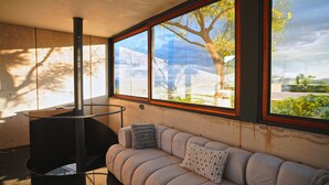 A modern interior with a sofa, a fireplace, and large windows offering a view of trees and a building. - Casa del Sol - CasaBlanca. Pool, privacy and mountain views (Oaxaca de Juárez)