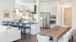 A modern kitchen with white cabinetry, a central island, and stainless steel appliances. - Prime Village Access | Walkable (Winter Park)