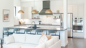 A modern kitchen with white cabinets, a central island with bar stools, stainless steel appliances, and pendant lighting. - Prime Village Access | Walkable (Winter Park)