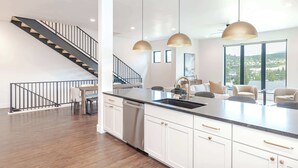 A modern kitchen with a central island, white cabinetry, and a staircase with black railings. - Prime Village Access | Walkable (Winter Park)