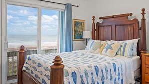 Une chambre avec une grande fenêtre donnant sur la plage, un cadre de lit en bois et une vue sur l’océan.