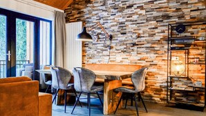 A dining area with a wooden table and chairs, a pendant lamp, and a brick-patterned wall. - Apartment Presseggersee Top 4 (Hermagor)