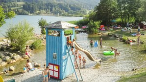 A water park with a blue play structure, a slide, and people enjoying the water. - Apartment Presseggersee Top 4 (Hermagor)