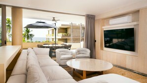 Quarto de hotel moderno com uma televisão grande, um sofá, uma mesa redonda e uma varanda com mobiliário de exterior.