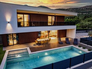 A modern two-story house with a swimming pool, outdoor seating, and a view of the surrounding landscape. - Luxury Villa Lueur with Pool (Mlini)