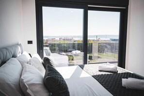 A modern bedroom with a large bed, a sofa, and a balcony with a view of the city. - Luxury Villa Lunero with Pool (Kaštel Stari)