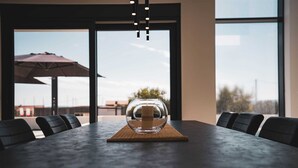 Une table de conférence surmontée d’un vase en verre transparent, entourée de chaises, dans une pièce dotée de grandes fenêtres et d’un parasol extérieur.