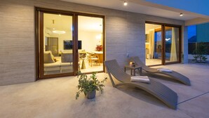 A modern outdoor lounge area with two reclining chairs, a small table, and a potted plant. - Villa Veluno with Pool (Kaštel Lukšić)
