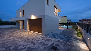 A modern two-story house with a large garage, a swimming pool, and a well-lit driveway. - Villa Veluno with Pool (Kaštel Lukšić)