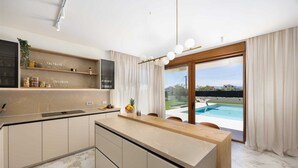 A modern kitchen with a marble countertop, built-in appliances, and a view of a swimming pool through large sliding glass doors. - Villa Veluno with Pool (Kaštel Lukšić)