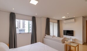 Ein Hotelzimmer mit Bett, Sofa, Fernseher und einem Fenster mit Vorhängen.