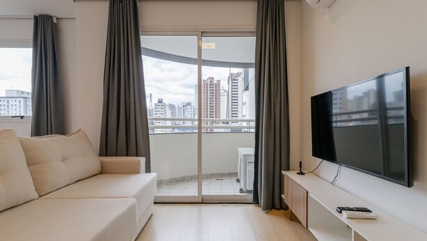 Een moderne woonkamer met een bank, een flatscreen televisie en een balkon met gordijnen.
