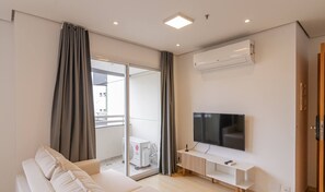 Ein modernes Wohnzimmer mit Flachbildfernseher, Sofa und einer Schiebeglastür, die auf einen Balkon führt.