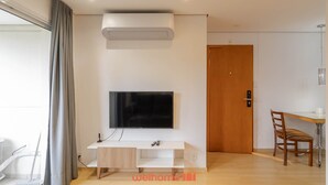 Een moderne woonkamer met een flatscreen-tv die aan een witte consoletafel is bevestigd, een luchtverwarmer die aan het plafond is gemonteerd, en een houten deur op de achtergrond.