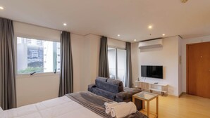 Een moderne hotelkamer met een groot bed, een bank, een televisie en een raam met gordijnen.