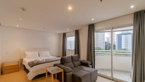 Een moderne hotelkamer met een groot bed, een sofa, een tafeltje en een balkon met uitzicht over de stad.