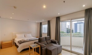 Ein modernes Hotelzimmer mit einem großen Bett, einer Couch, einem kleinen Tisch und einem Balkon mit Blick auf die Stadt.