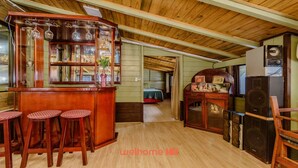 Een gezellige, rustieke keuken met houten balken, een bar met krukken, en een slaapkamer met een bed en een kaptafel.