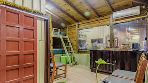 Een gezellig cabin interieur met een houten plafond, een rode deur, een stapelbed, een klein bureau en een stoel.