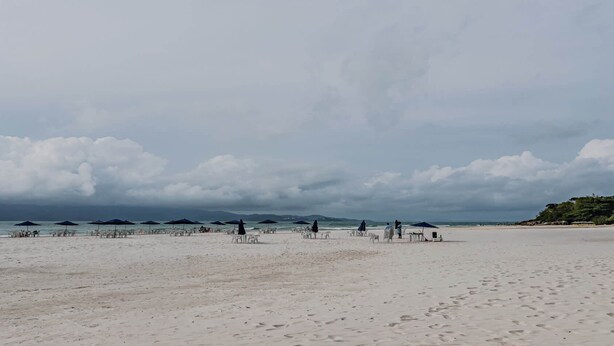 Een strand met parasols en stoelen, een zandstrand en een bewolkte lucht.