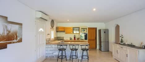A kitchen with a central island, bar stools, a refrigerator, and a clock on the wall.