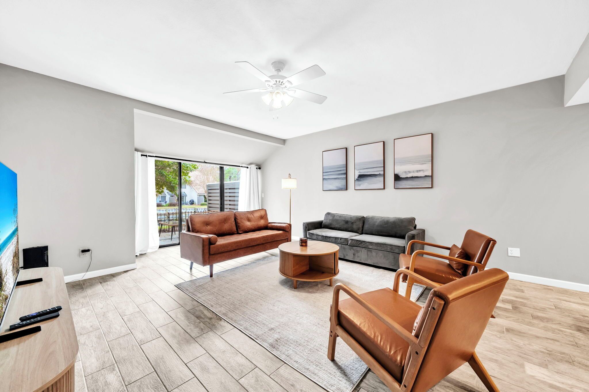 A spacious living room with a large window, a ceiling fan, and a flat-screen TV.
