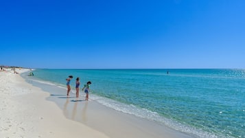 A beach with clear blue water and a few people standing by the shore.
