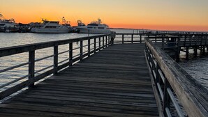 Une jetée en bois s’étendant dans des eaux calmes au coucher du soleil, avec plusieurs yachts amarrés à proximité.