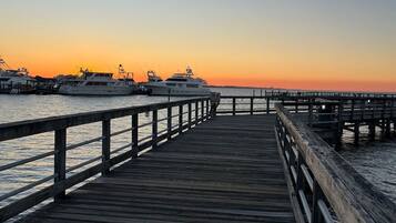 A wooden pier extending into calm waters at sunset, with several yachts docked nearby.