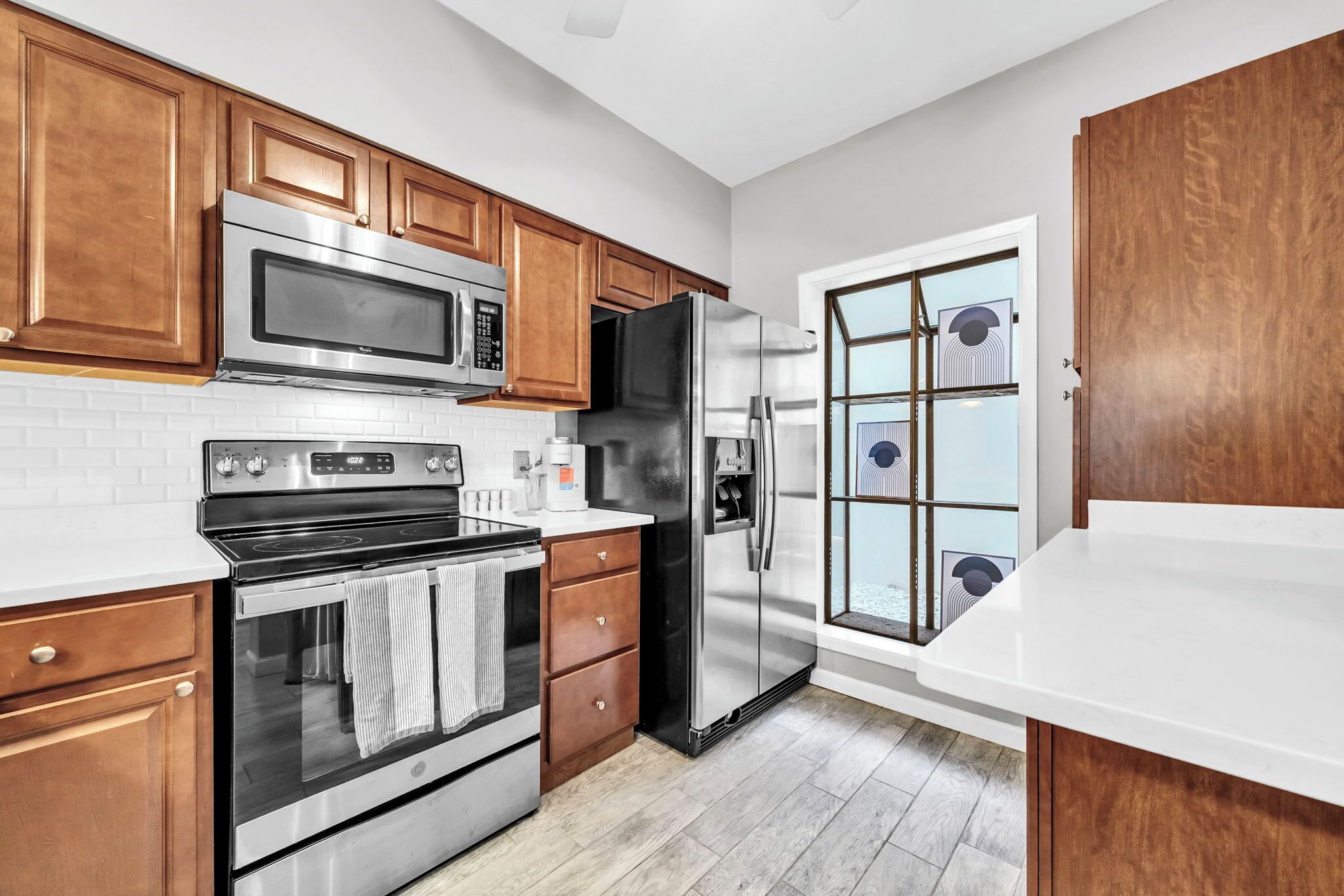 A modern kitchen with stainless steel appliances, wooden cabinets, and a white countertop.