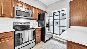 Une cuisine moderne dotée d’appareils électroménagers en acier inoxydable, de meubles en bois et d’un plan de travail blanc.