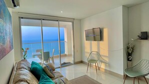 Ein modernes Wohnzimmer mit Ledersofa, Flachbildfernseher und Meerblick durch große Schiebetüren.