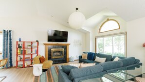A modern living room with a fireplace, a large sofa, a glass coffee table, and a bookshelf. - Family Retreat for 14 - Hot tub, Sauna, Golf Simulator, Arcade (Ankeny)