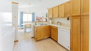 A modern kitchen with wooden cabinets, a white countertop, and a built-in dishwasher. - Family Retreat for 14 - Hot tub, Sauna, Golf Simulator, Arcade (Ankeny)