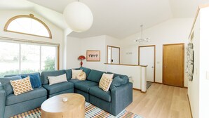 A modern living room with a sectional sofa, a wooden coffee table, and patterned rugs. - Family Retreat for 14 - Hot tub, Sauna, Golf Simulator, Arcade (Ankeny)