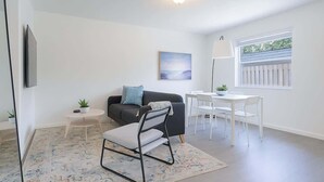 Un salon moderne avec un canapé noir, une table à manger blanche et une petite table d’appoint agrémentée d’une plante.