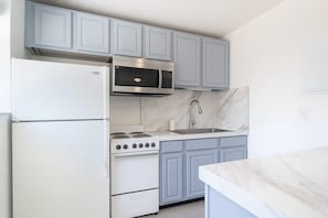 Une cuisine avec des meubles de couleur bleu clair, un réfrigérateur blanc, un four à micro-ondes en acier inoxydable, une cuisinière à gaz et un plan de travail en marbre.