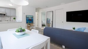 Un salon moderne avec une table blanche, un canapé bleu et un téléviseur à écran plat fixé au mur.