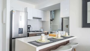 A modern kitchen with white cabinetry, a stainless steel refrigerator, a gas stove, and a dining area with a white island and bar stools. - Sight 1707 · Ocean View 2BR Stylish Apt • Pool, Gym & Parking (Lima)