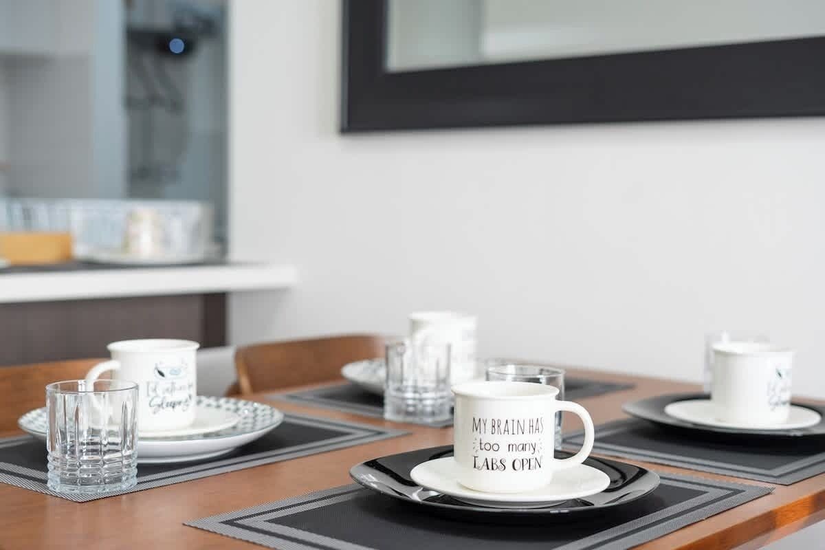 A dining table set with white cups and saucers, some with text, and clear glasses.