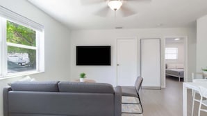 Un salon moderne avec un canapé gris, un téléviseur à écran plat et un ventilateur de plafond.